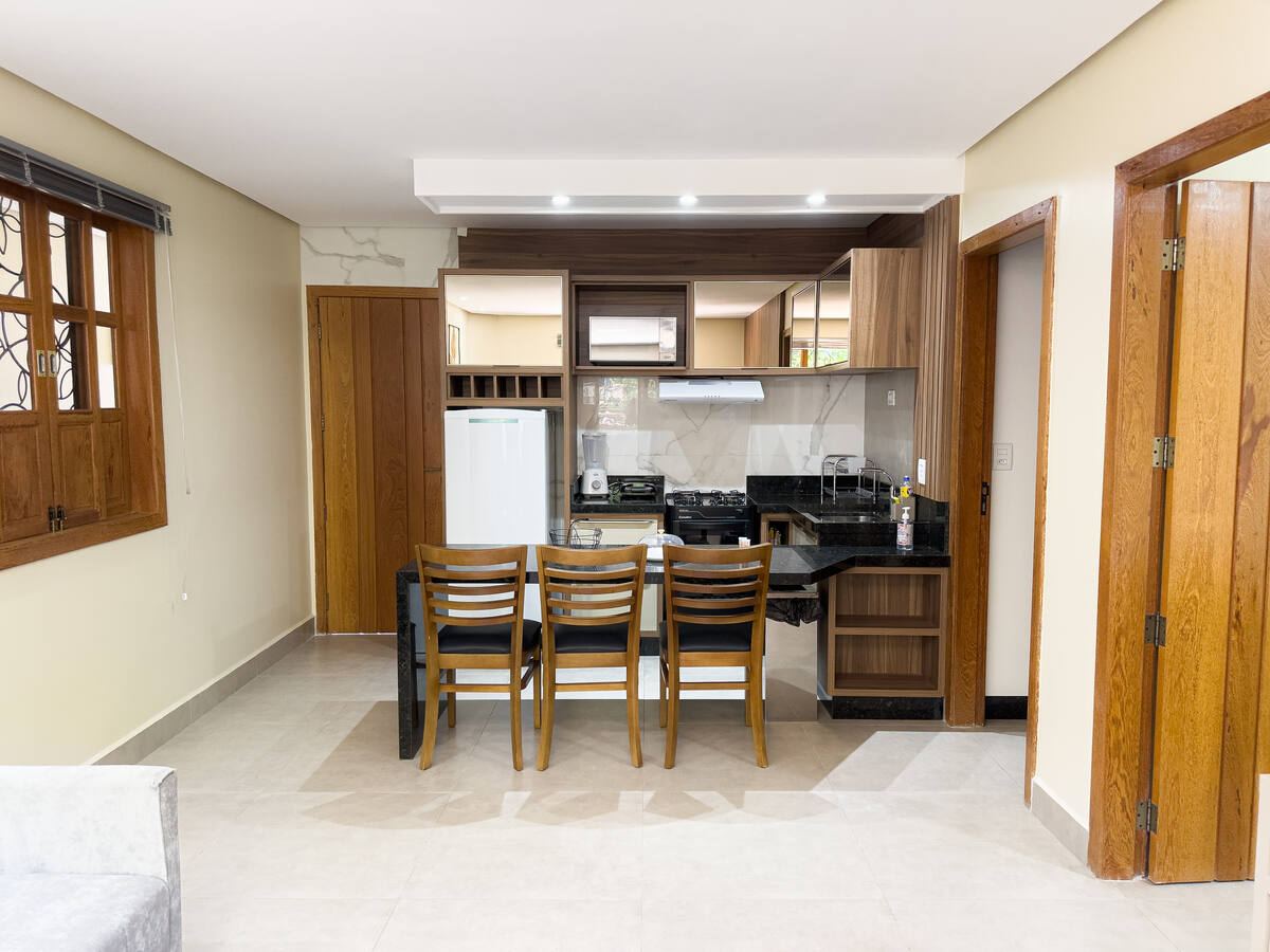 Sala do flat com mesa de jantar, a cozinha ao fundo e portas de madeira